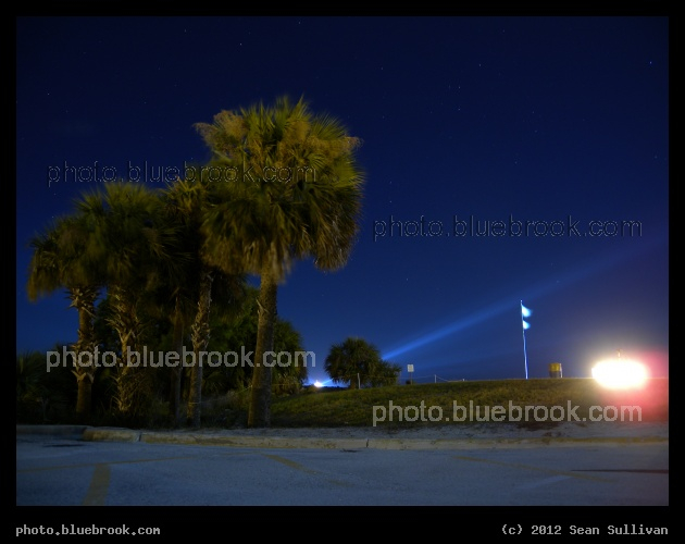 Prelude to Launch - On the night before the final launch of space shuttle Endeavour, from the parking lot at the Kennedy Space Center press site, the xenon floodlights light up the sky, and the countdown clock is brilliant beside the flag