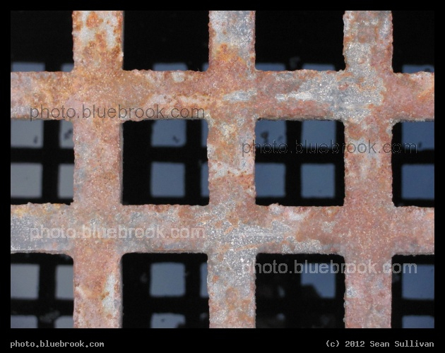 Grid - Looking down at a metal grate covering a stormwater drain, and in the background a reflection of the sky in water below, Dover NH